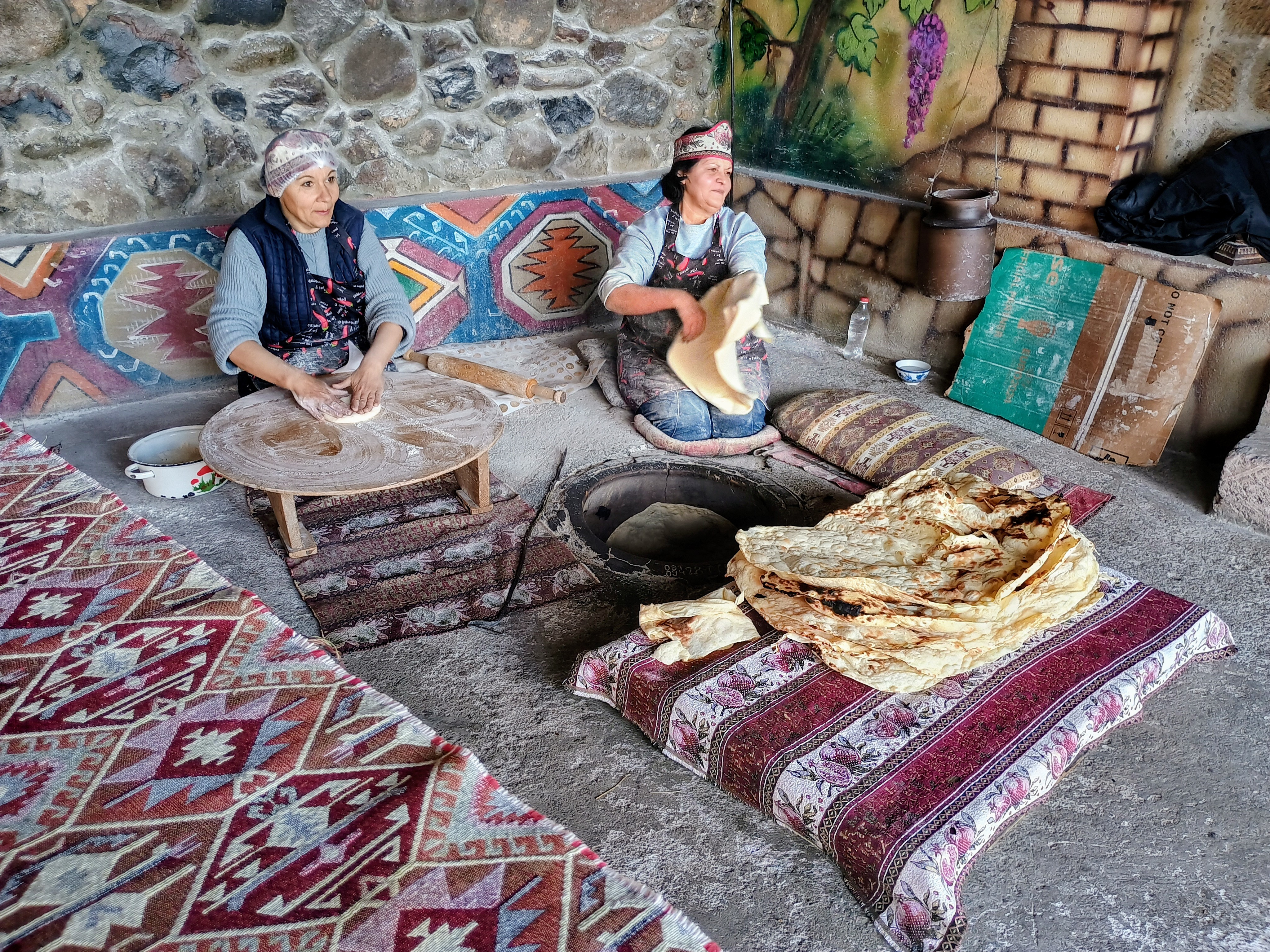 Two women baking traditional Armenian lavash bread in a stone tonir oven