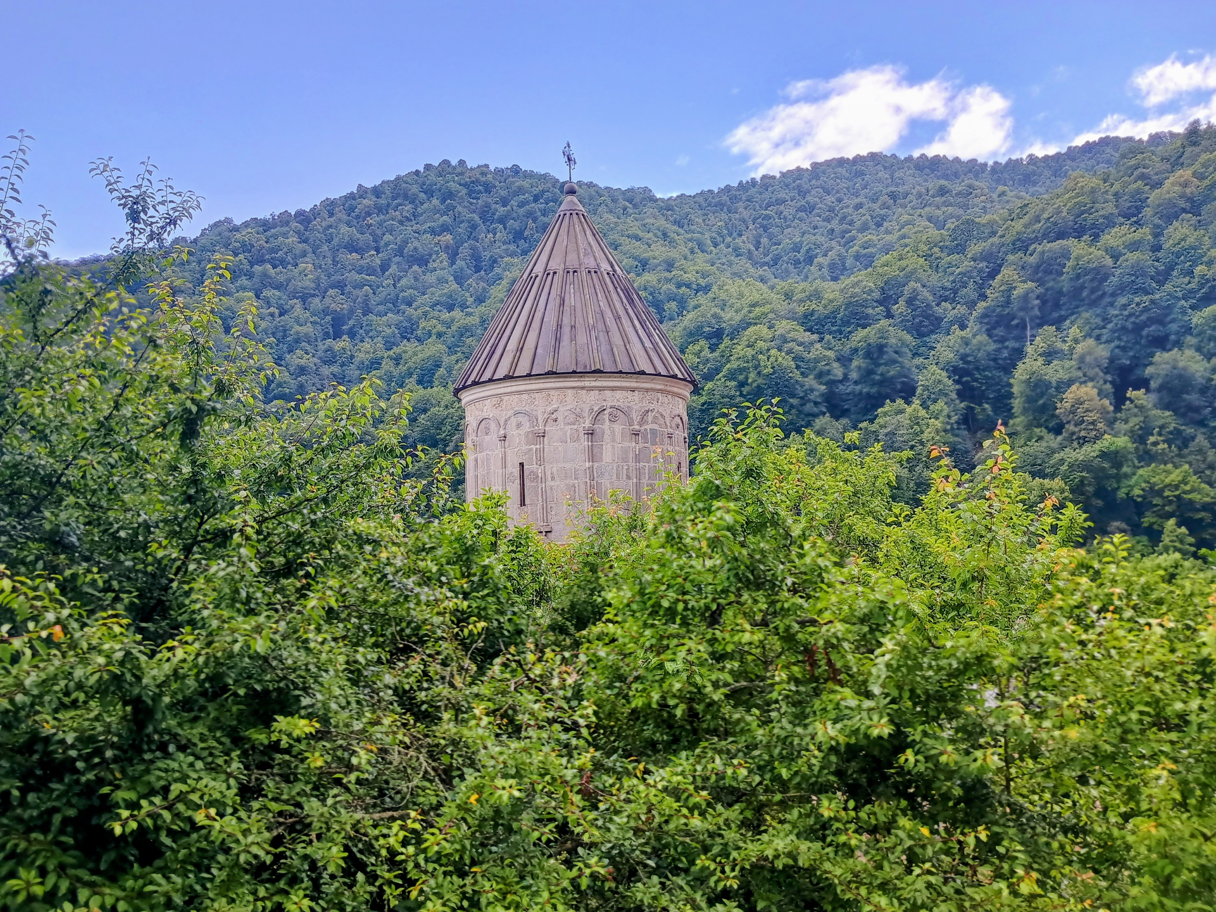 The conical stone roof of an Armenian monastery surrounded by forested mountains